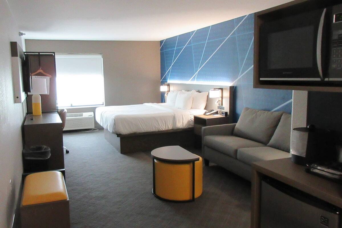 A hotel room with a bed, a sofa, a desk, a television, and a window.