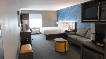 A hotel room with a bed, a sofa, a desk, a television, and a window.