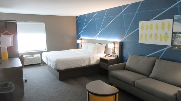 A hotel room with a bed, a sofa, a desk, a lamp, a phone, and a wall with a geometric pattern. - Comfort Inn & Suites Grand Forks near Alerus Center (Grand Forks)