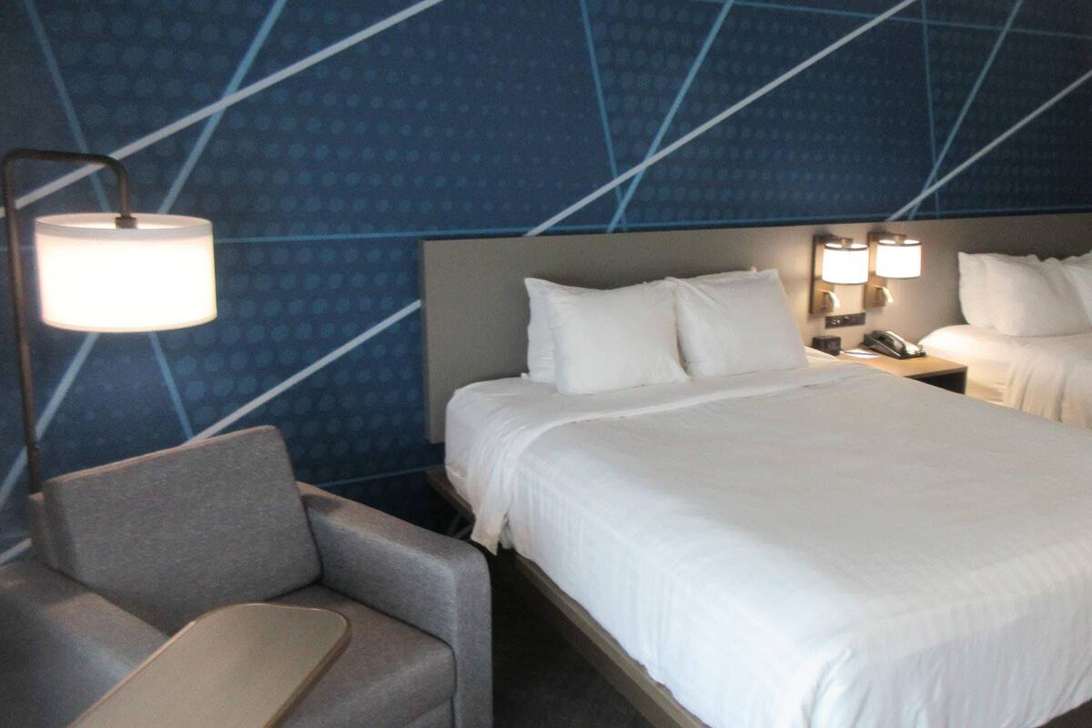 A hotel room with two beds, a desk, a chair, and a wall with a geometric pattern.