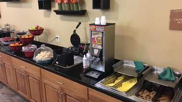 A buffet setup with various food items, a waffle maker, and a beverage dispenser.