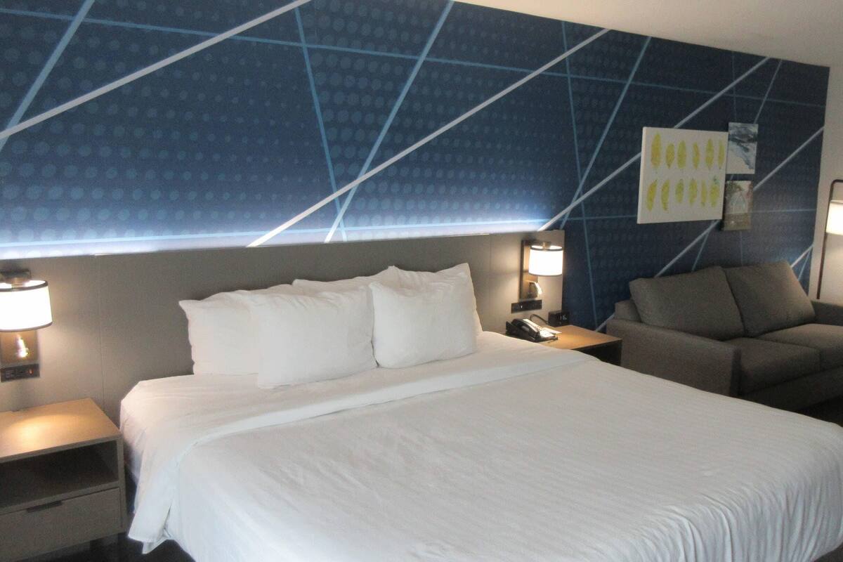 A hotel room with a large bed, two bedside tables, a sofa, and a wall with a geometric pattern.