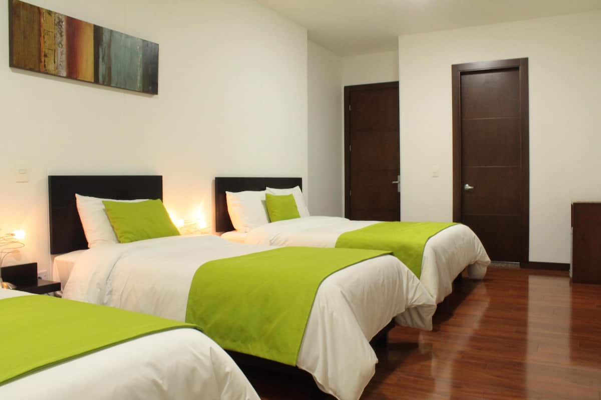 Habitación de hotel con dos camas, cada una con ropa de cama verde y blanca, suelo de madera y un cuadro en la pared.