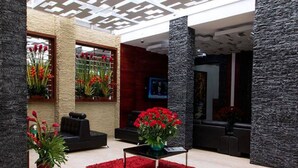 A modern lobby with a geometric ceiling design, stone pillars, and red floral arrangements. - Hotel Macao Colombia (Bogotá)