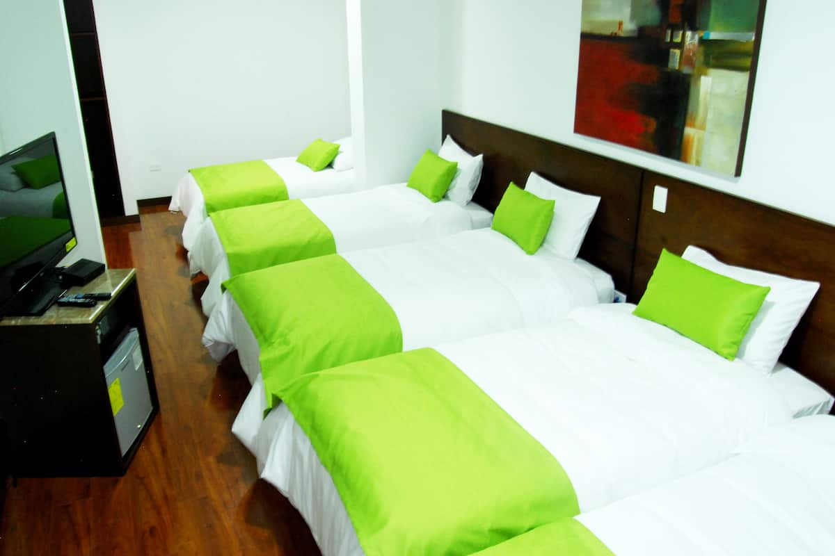 Habitación de hotel con cuatro camas individuales, cada una con ropa de cama verde y blanca. Hay un escritorio con una computadora y un teléfono.