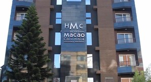 Monikerroksinen hotellirakennus, jonka julkisivussa on selkeästi näkyvissä kyltti, jossa lukee: ”HMC Hotel Macao Colombia”.