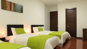 A hotel room with three beds, each with white bedding and green accents, a wooden floor, and a dark wooden door. - Hotel Macao Colombia (Bogotá)