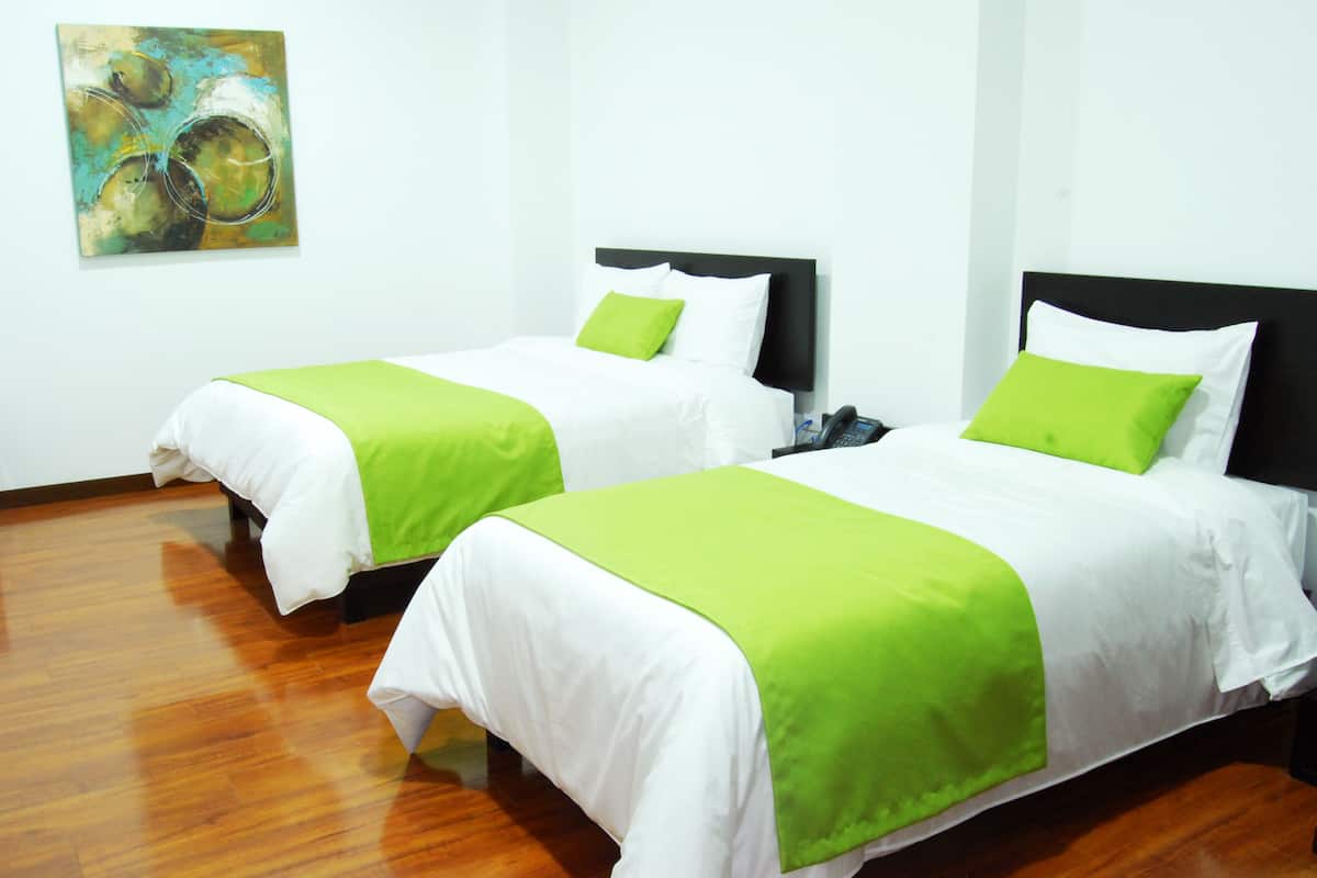 Dos camas individuales con ropa de cama blanca y verde, un suelo de madera y un cuadro en la pared.