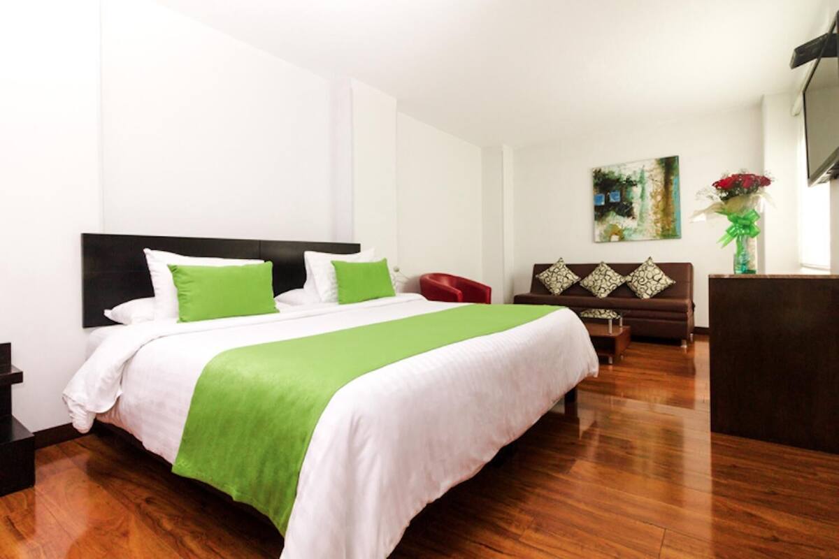 Una habitación de hotel con una cama grande, un sofá marrón, una mesita y un cuadro en la pared.