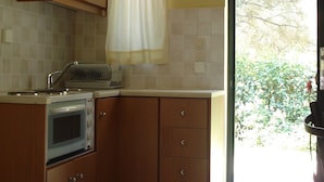 A compact kitchen with wooden cabinets, a built-in oven, and a window with a curtain. - Ionian Breeze Studios (Lefkada)