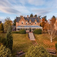 Una casa grande con un invernadero, un césped cuidado y un cielo despejado.