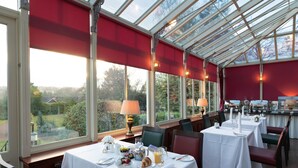 A conservatory dining area with tables set for breakfast, large windows, and a view of the garden. - Lochardil House Hotel (Inverness)
