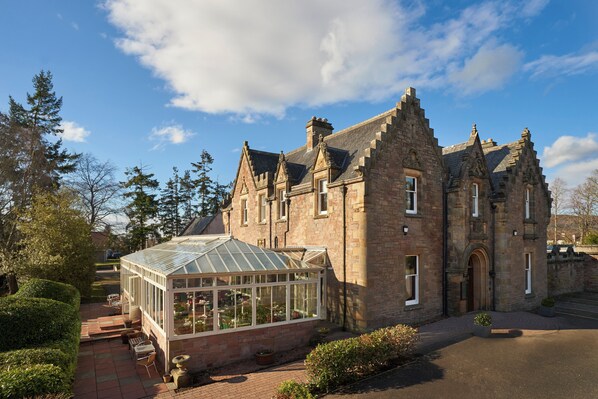 A historic building with a conservatory, stone walls, and a clear sky. - Lochardil House Hotel (Inverness)