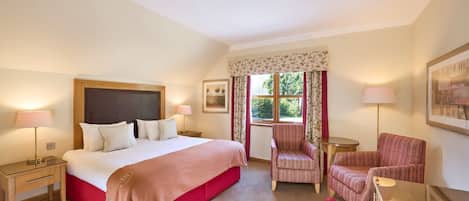 Une chambre d’hôtel avec un grand lit, deux tables de chevet, une chaise, un bureau et une fenêtre avec des rideaux.