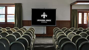 A conference room with rows of chairs, a projection screen, and a logo for Lochardil House Innermess.