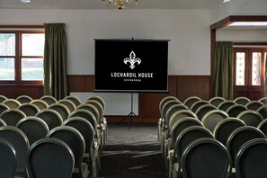 Ein Konferenzraum mit Reihen von Stühlen und einem Projektionsschirm, sowie dem Logo von Lochardil House Innermess.