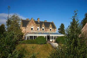 A large stone building with a conservatory, surrounded by greenery. - Lochardil House Hotel (Inverness)