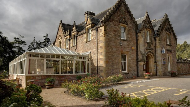 A historic stone building with a conservatory, a driveway, and a parking area marked with a wheelchair symbol. - Lochardil House Hotel (Inverness)