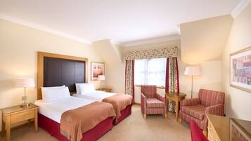 A hotel room with two beds, a sitting area with a chair and a table, and a large window with curtains.