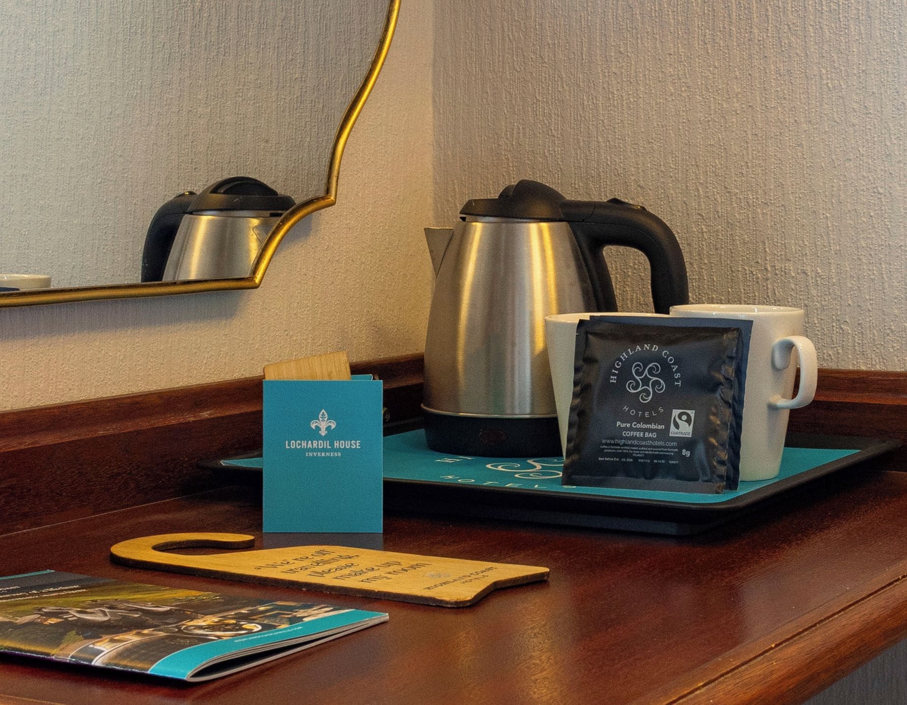 Een hotelkamer met een koffiezetapparaat, een kop, een zak koffie, een menukaart en een tijdschrift op de tafel.