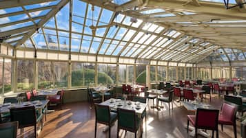 A spacious conservatory with multiple dining tables and chairs, large windows, and a high ceiling.