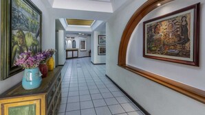 A hallway with tiled flooring, framed artwork on the walls, and a wooden cabinet with a vase of flowers.