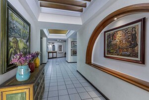 A hallway with tiled flooring, framed artwork on the walls, and a wooden cabinet with a vase of flowers.