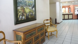 A hallway with a framed painting, wooden furniture, and a reception area in the background.