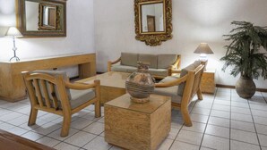 A room with a wooden sofa, two wooden chairs, a glass coffee table, a vase, a lamp, a mirror, and a potted plant.