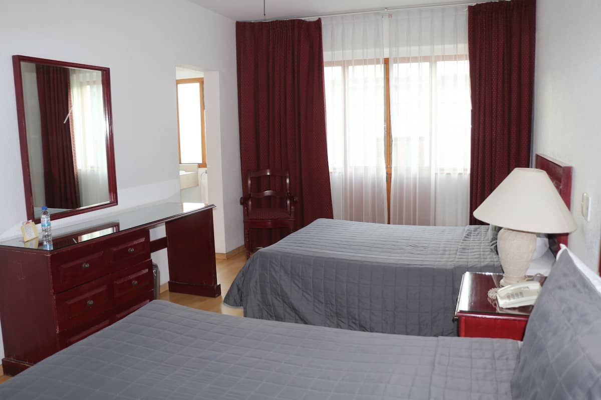 Habitación de hotel con dos camas, un escritorio, una silla, un espejo, una lámpara y un teléfono.