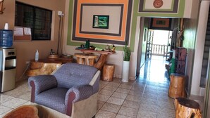 A room with a blue sofa, wooden stools, a water dispenser, and a wall with geometric patterns. - Hotel La Escalinata (Copan Ruinas)