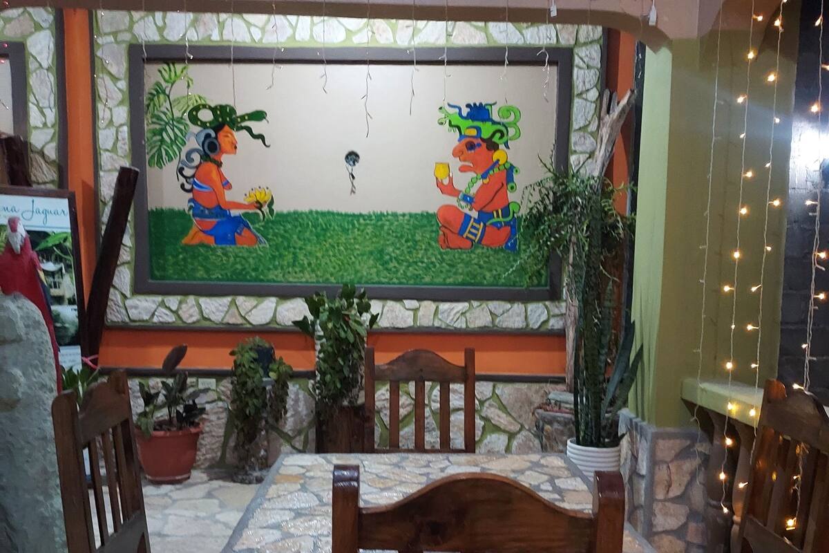 A restaurant interior with wooden chairs, a stone-tiled floor, and a mural on the wall.