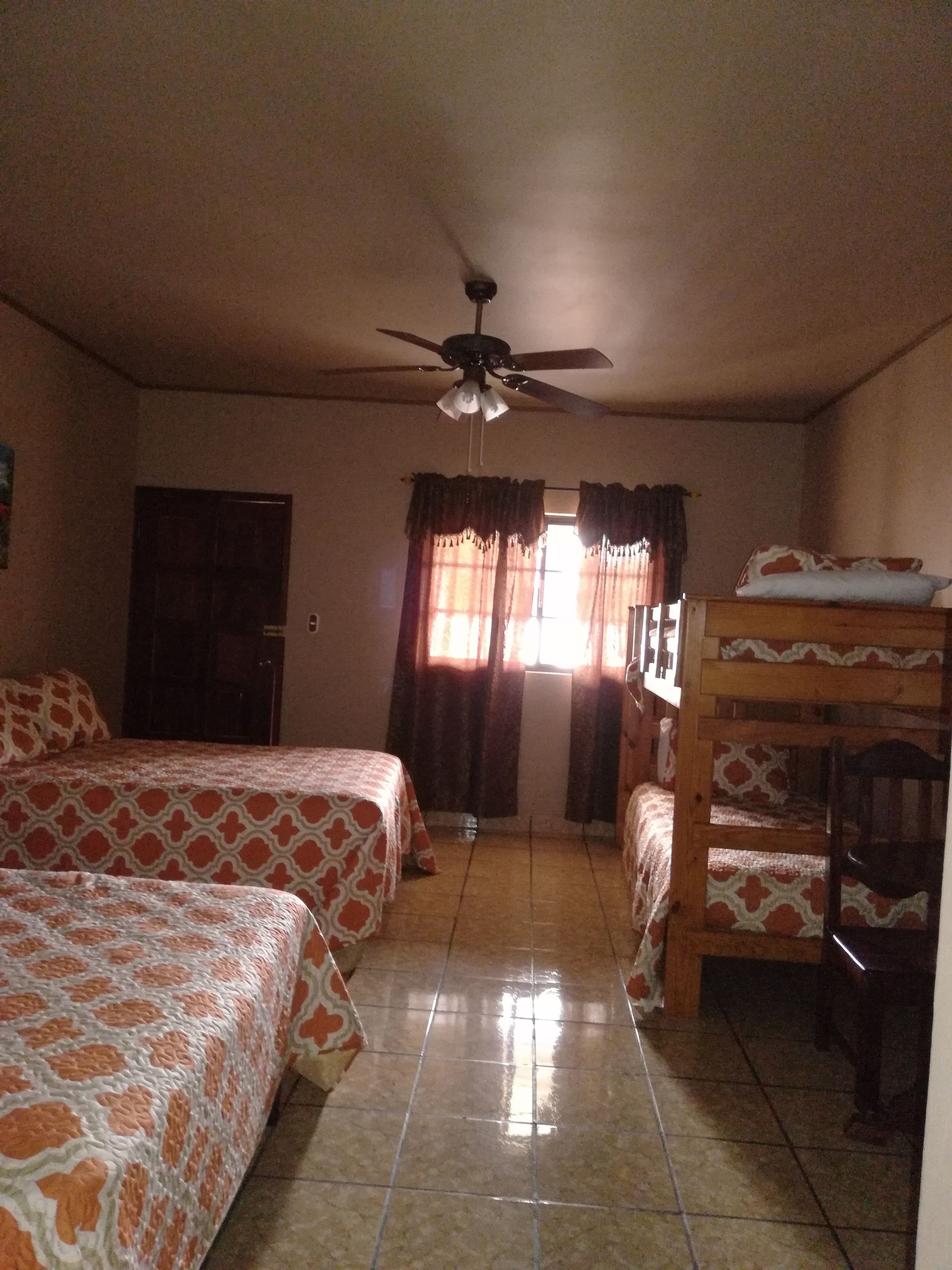 A room with two beds, a ceiling fan, a window with curtains, and a bunk bed.