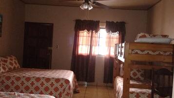 A room with two beds, a ceiling fan, a window with curtains, and a bunk bed.