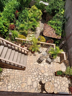 A stone-paved courtyard with a wooden staircase, potted plants, and outdoor seating.