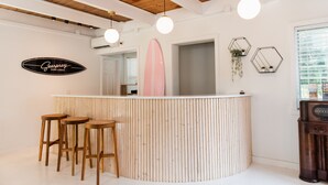 A surf lodge bar with wooden stools, a surfboard, and hexagonal wall decorations. - Seaspray Surf Lodge (Vero Beach)