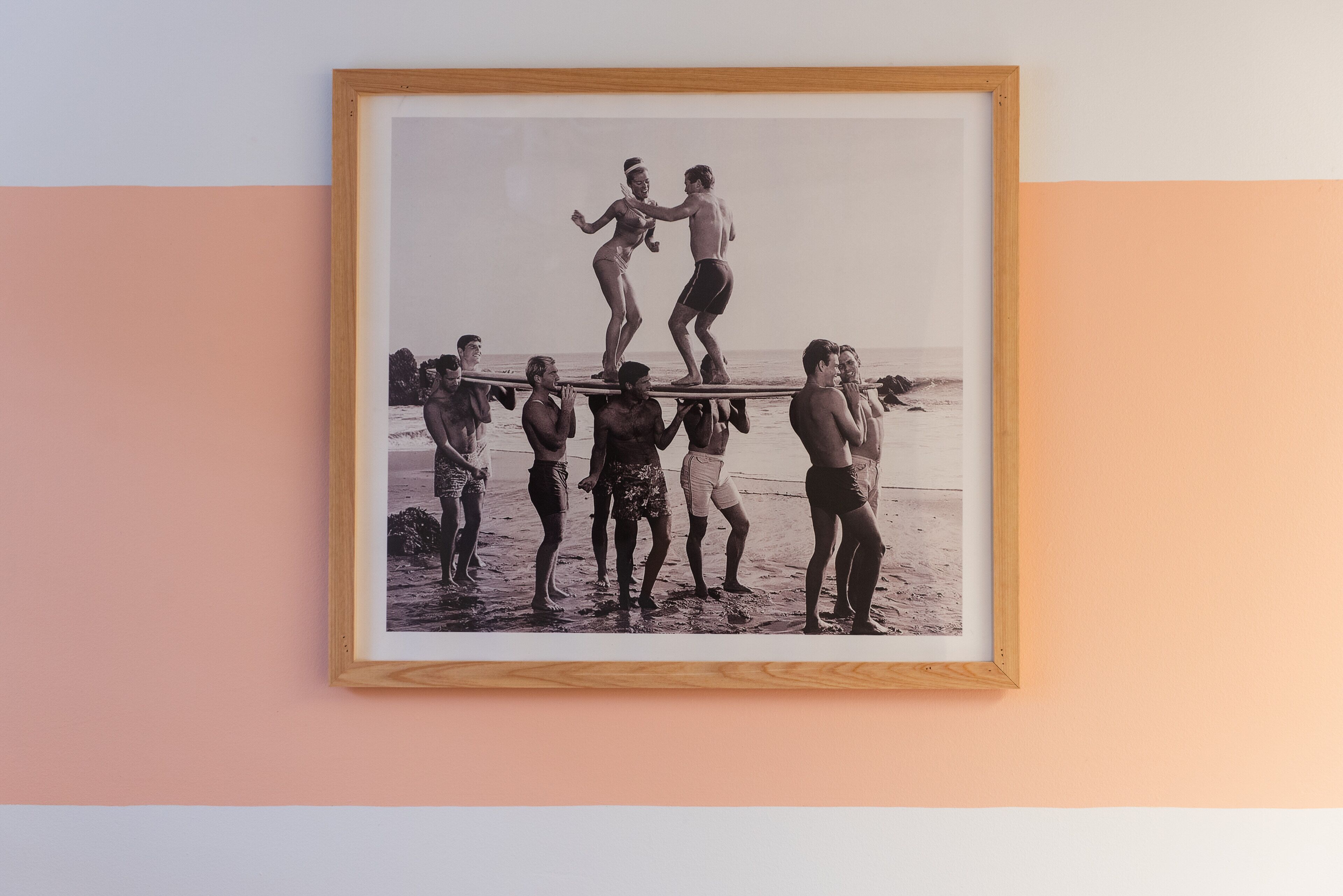 A framed photograph of a beach scene with people standing on a surfboard.