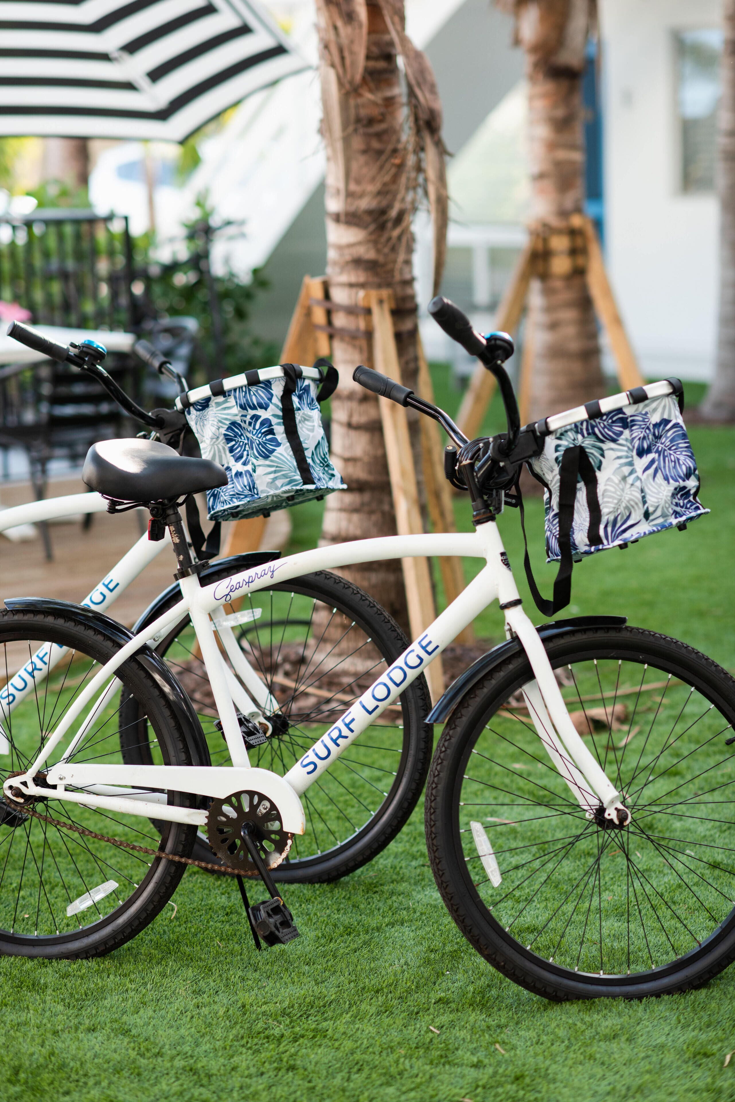A white bicycle with a basket and a bag attached, parked on grass.