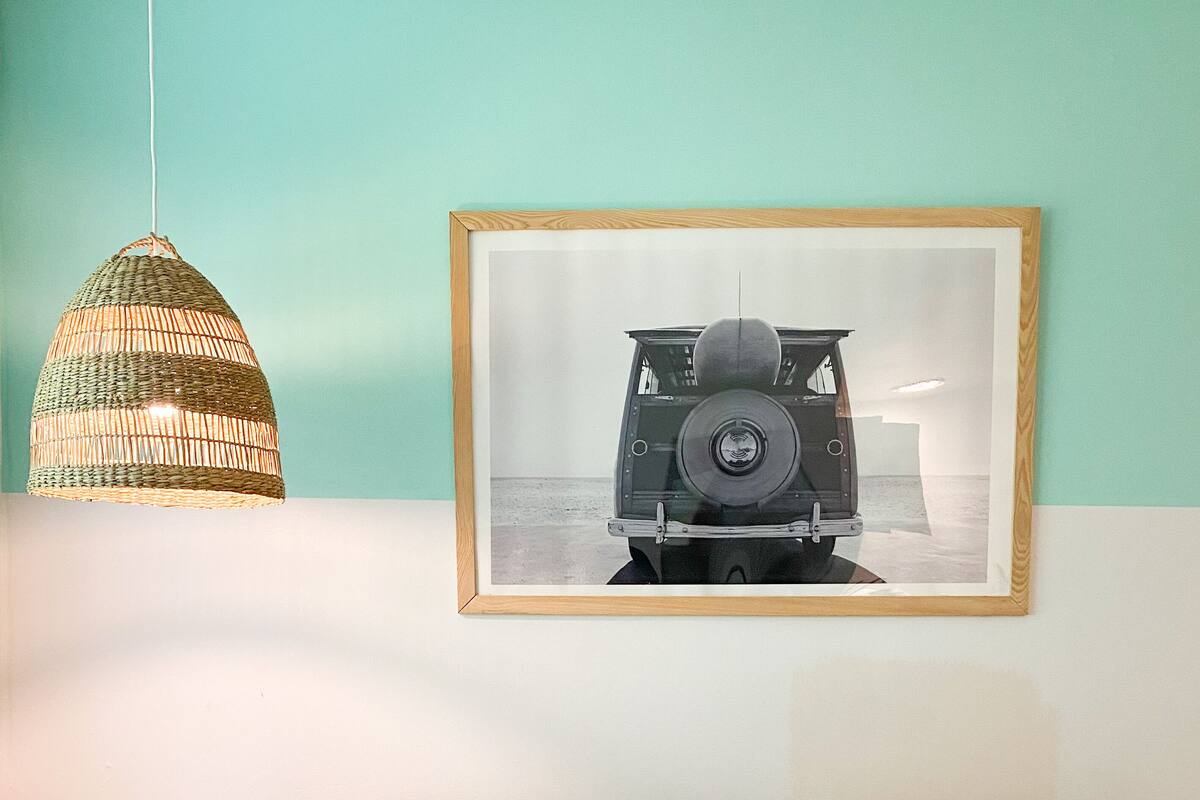 A neatly made bed with white bedding, a #SSSL pillow, and a framed picture of a vintage car on the wall.