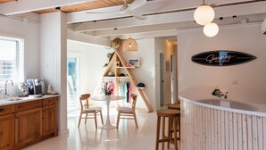 A modern kitchen with wooden cabinets, a dining area with a round table and chairs, and a bar area with stools. - Seaspray Surf Lodge (Vero Beach)