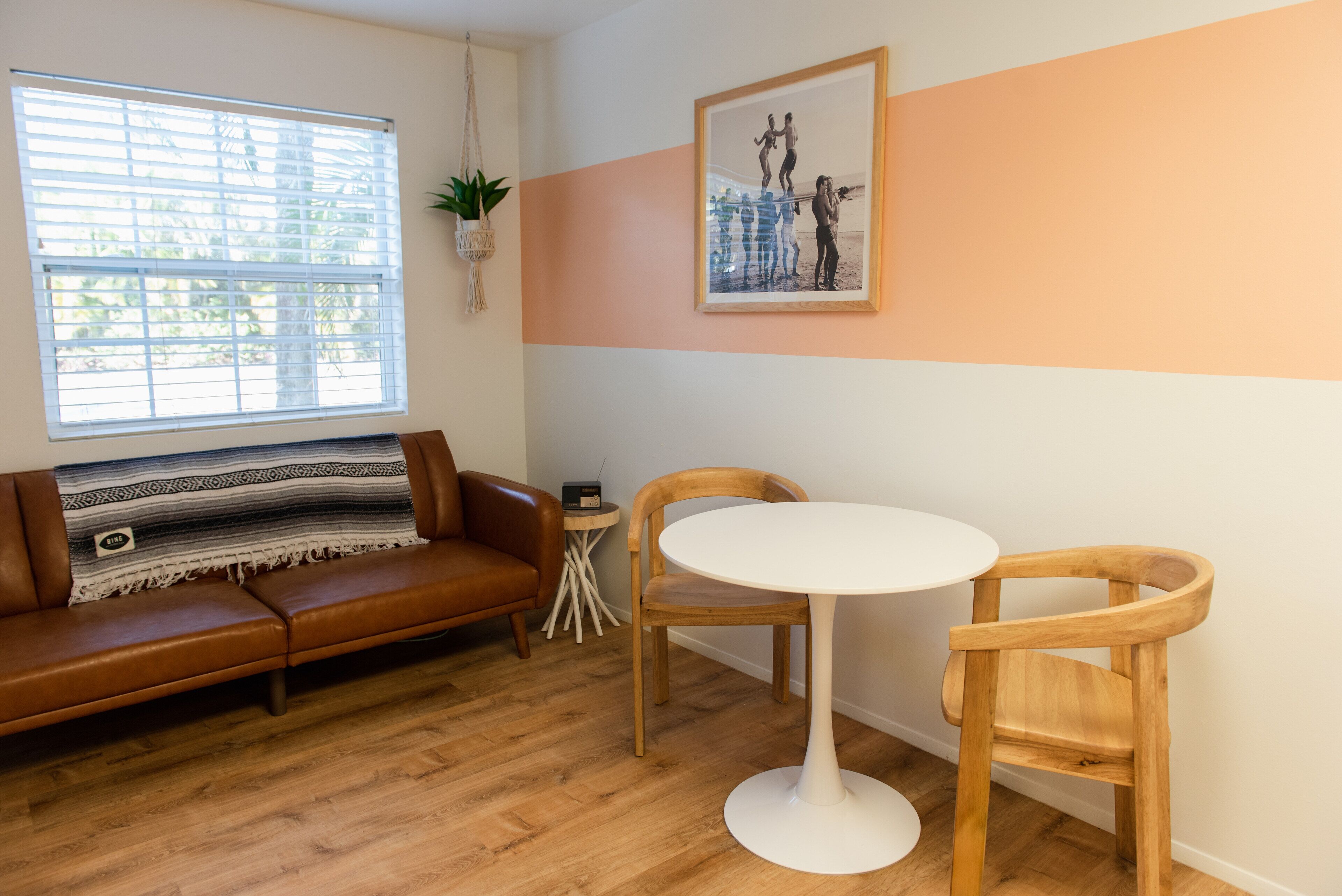 Un salon avec un canapé en cuir marron, une table ronde blanche et deux chaises en bois.