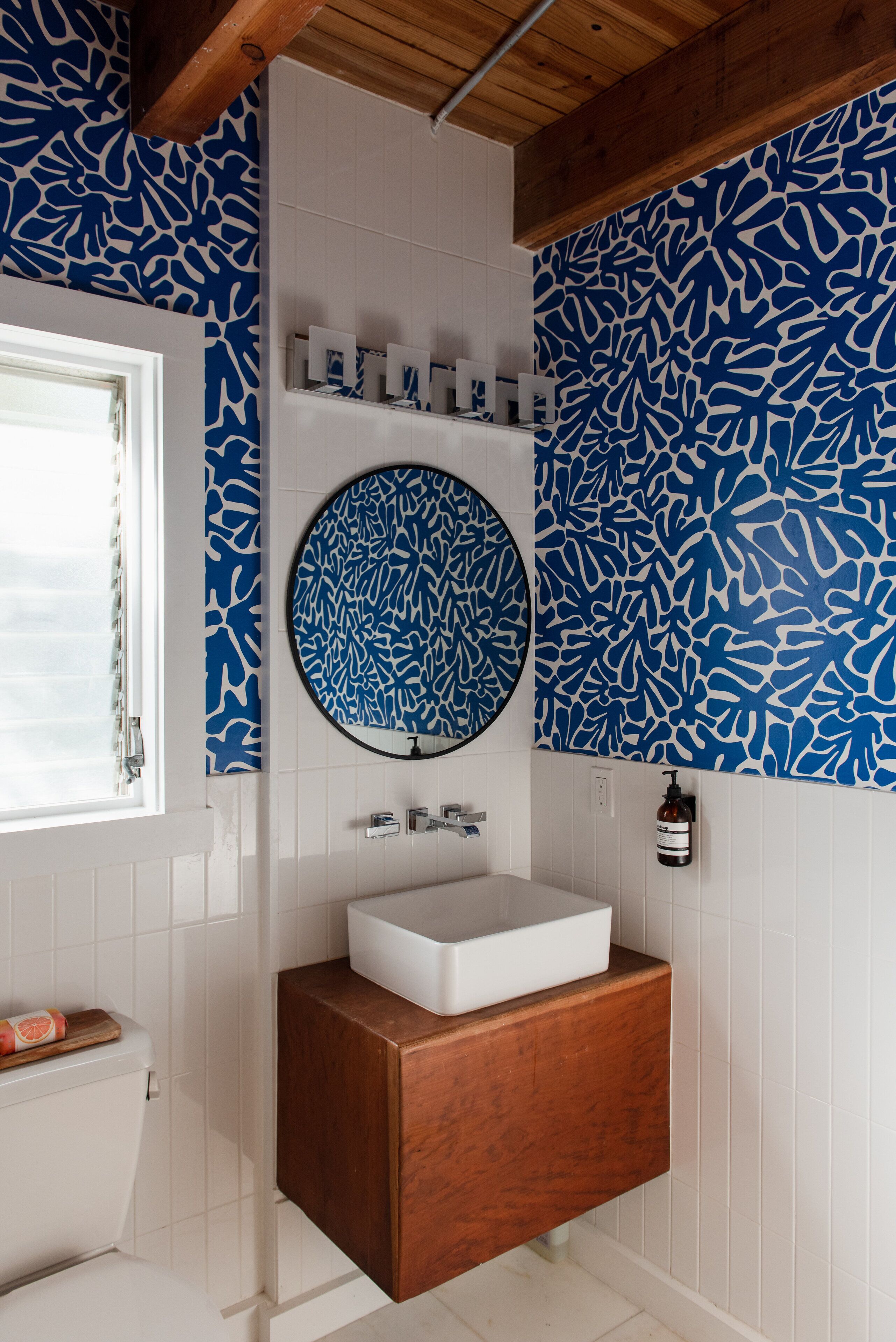 Une salle de bain avec un lavabo blanc, un meuble-lavabo en bois et un mur orné d’un motif bleu.