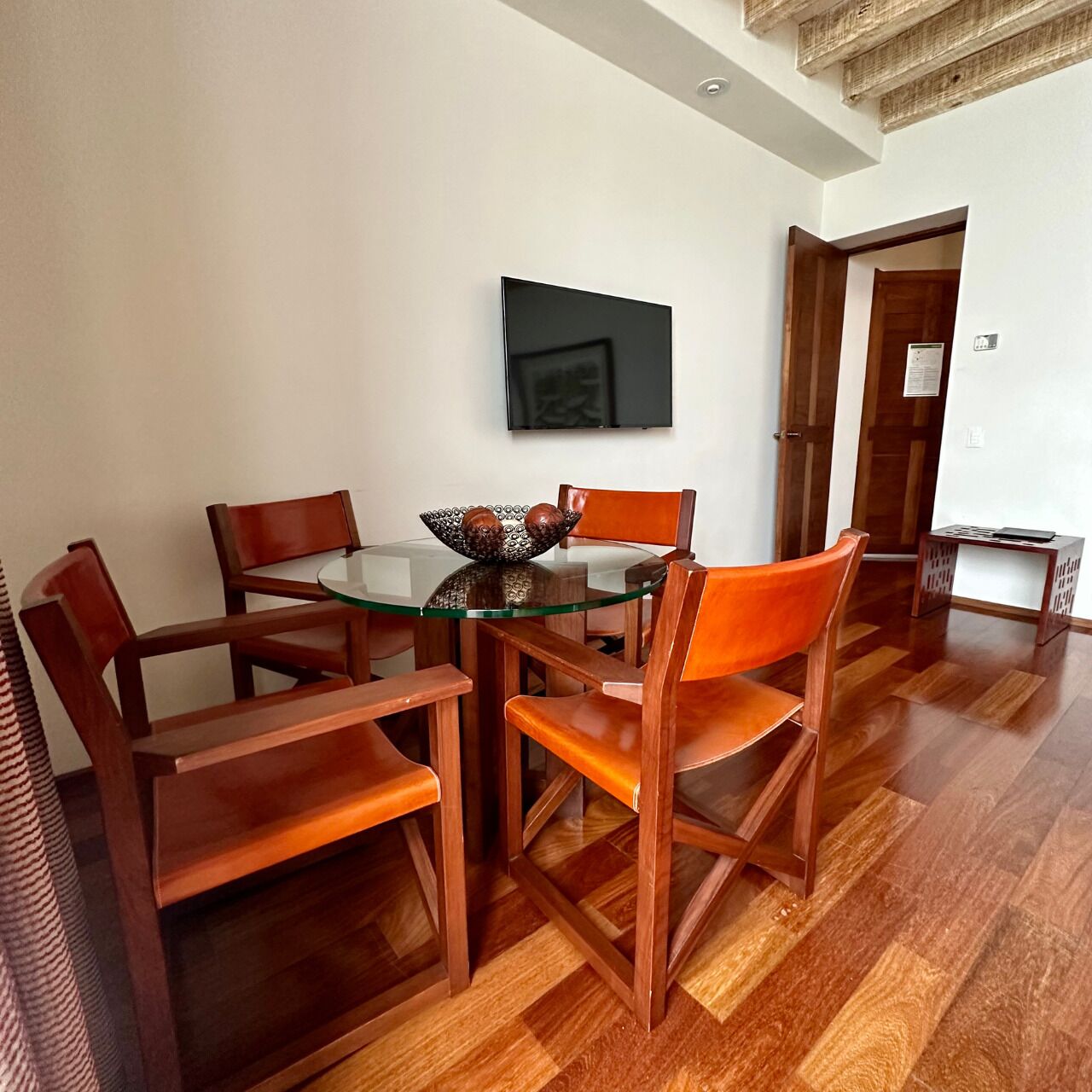 Un comedor con una mesa de vidrio rodeada de sillas de madera, un cuenco decorativo sobre la mesa y un televisor de pantalla plana montado en la pared.