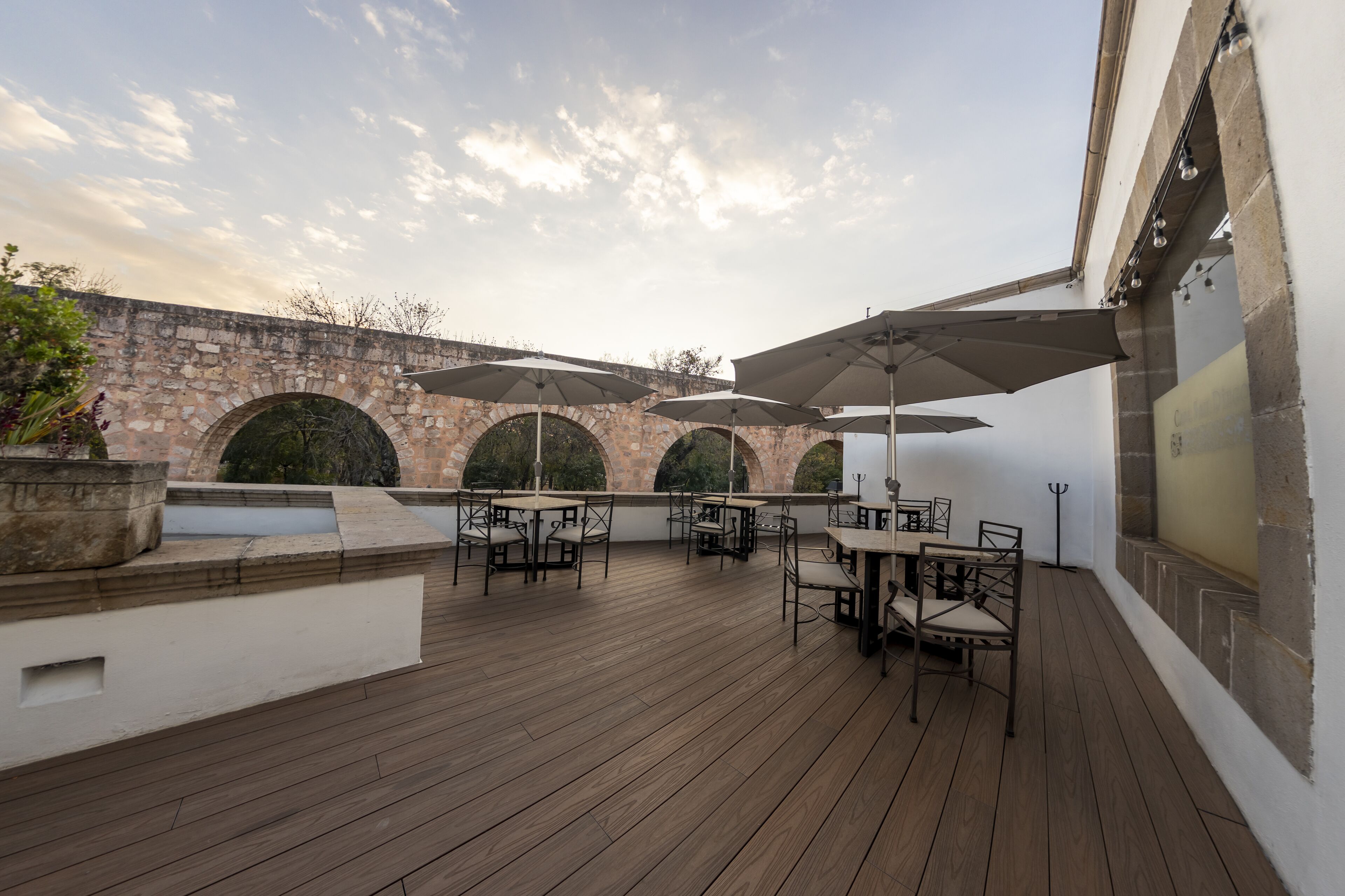 An outdoor patio with wooden flooring, stone arches, and tables with umbrellas.