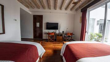 A hotel room with two beds, a TV, a desk with chairs, and a window with a view.