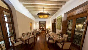 A dining area with wooden tables and chairs, a chandelier, and a view through a window. - Hotel Boutique Casa San Diego (Morelia)