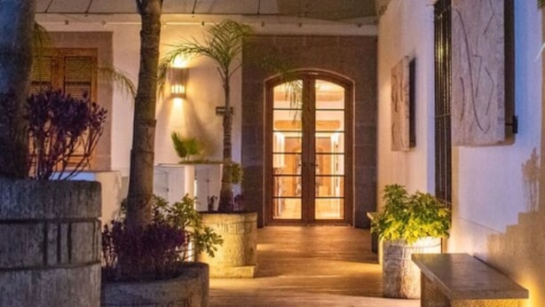 A wooden pathway leading to a glass door entrance, surrounded by potted plants and a stone bench. - Hotel Boutique Casa San Diego (Morelia)
