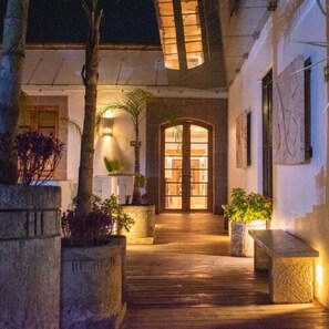 A wooden pathway leading to a glass door entrance, surrounded by potted plants and a stone bench. - Hotel Boutique Casa San Diego (Morelia)