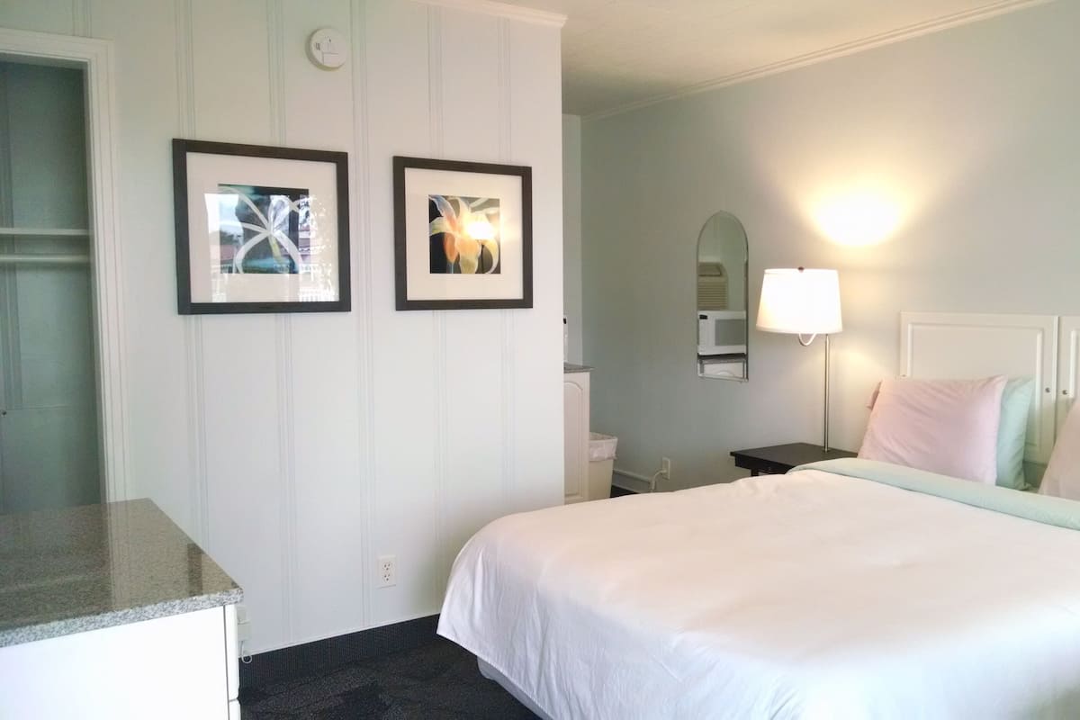 A hotel room with a bed, a nightstand, a lamp, a mirror, and two framed pictures on the wall.