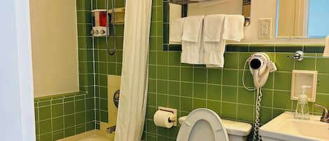 Baño con bañera, inodoro y ducha. Toallas apiladas en un estante, secador de manos y cubo de basura.